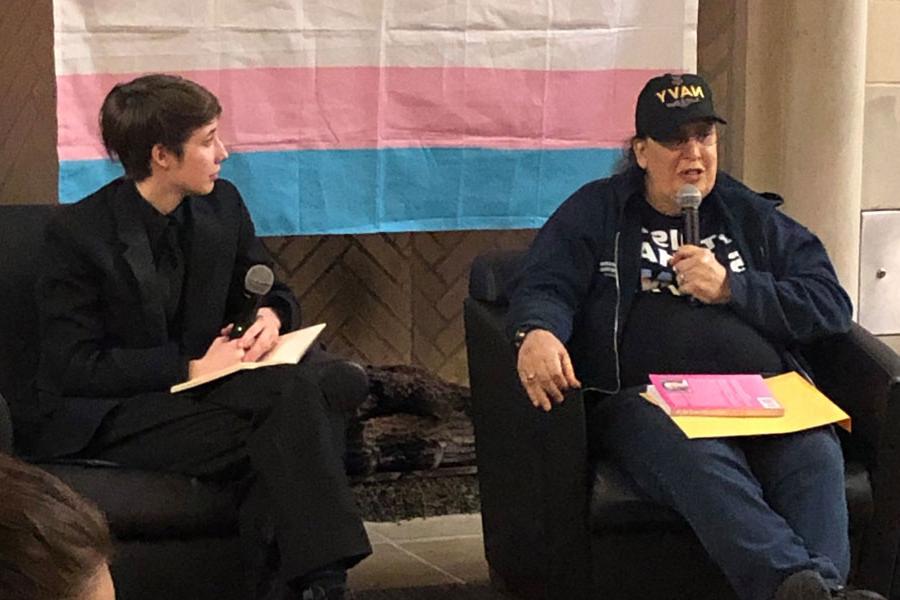 Two people sit in front of the 变性人 pride flag and address an audience.